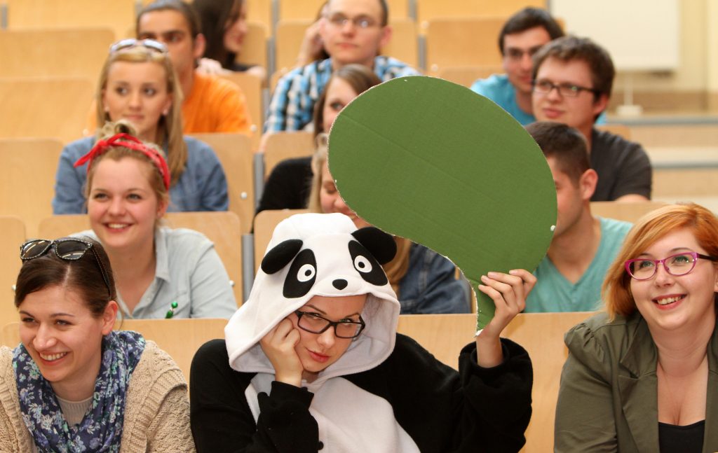 studenci w sali wykładowej z studentką przebraną za zawierzaka w tle